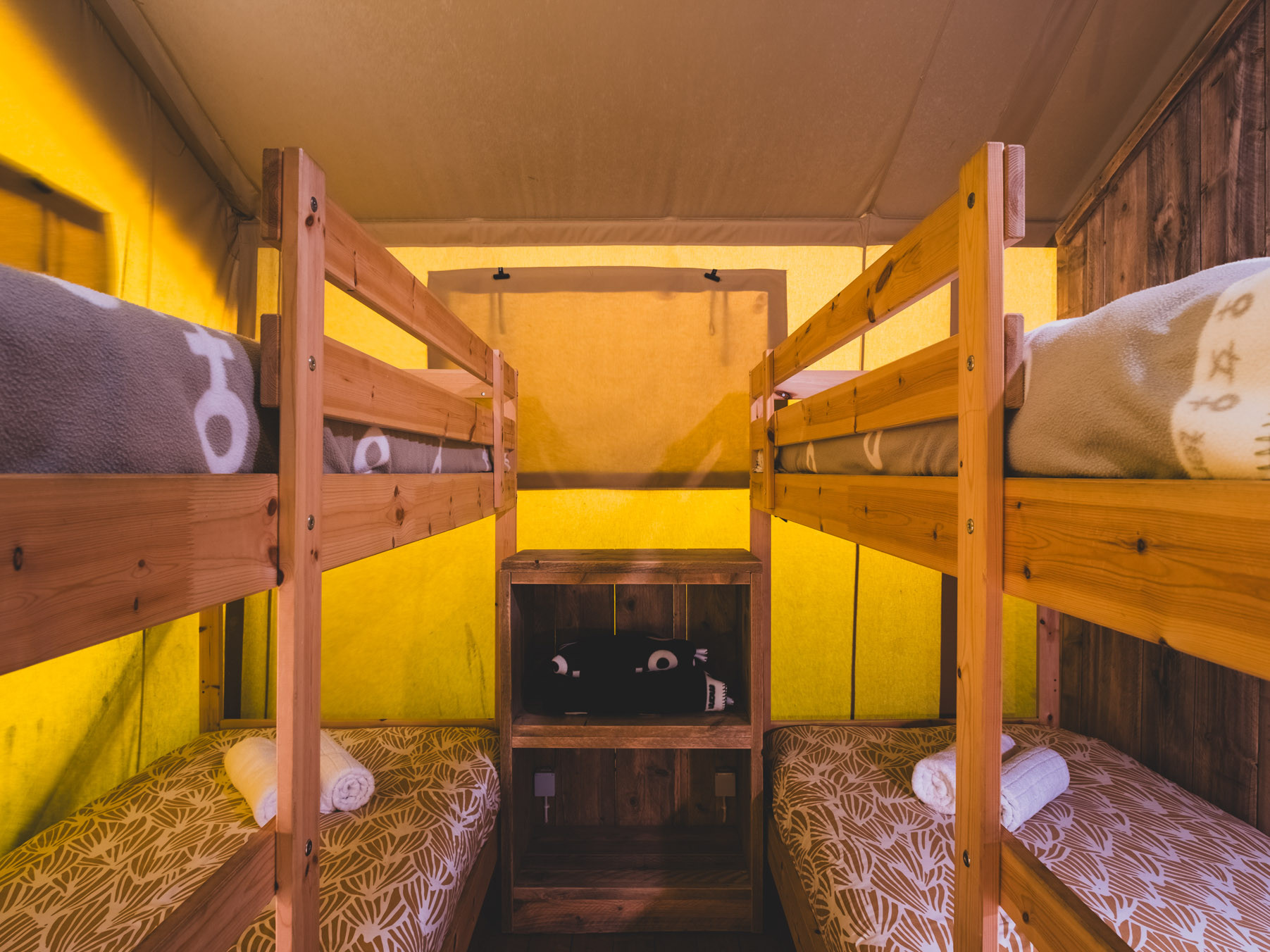 Small room with two wooden bunk beds, patterned mattresses, rolled towels, and a small wooden cabinet