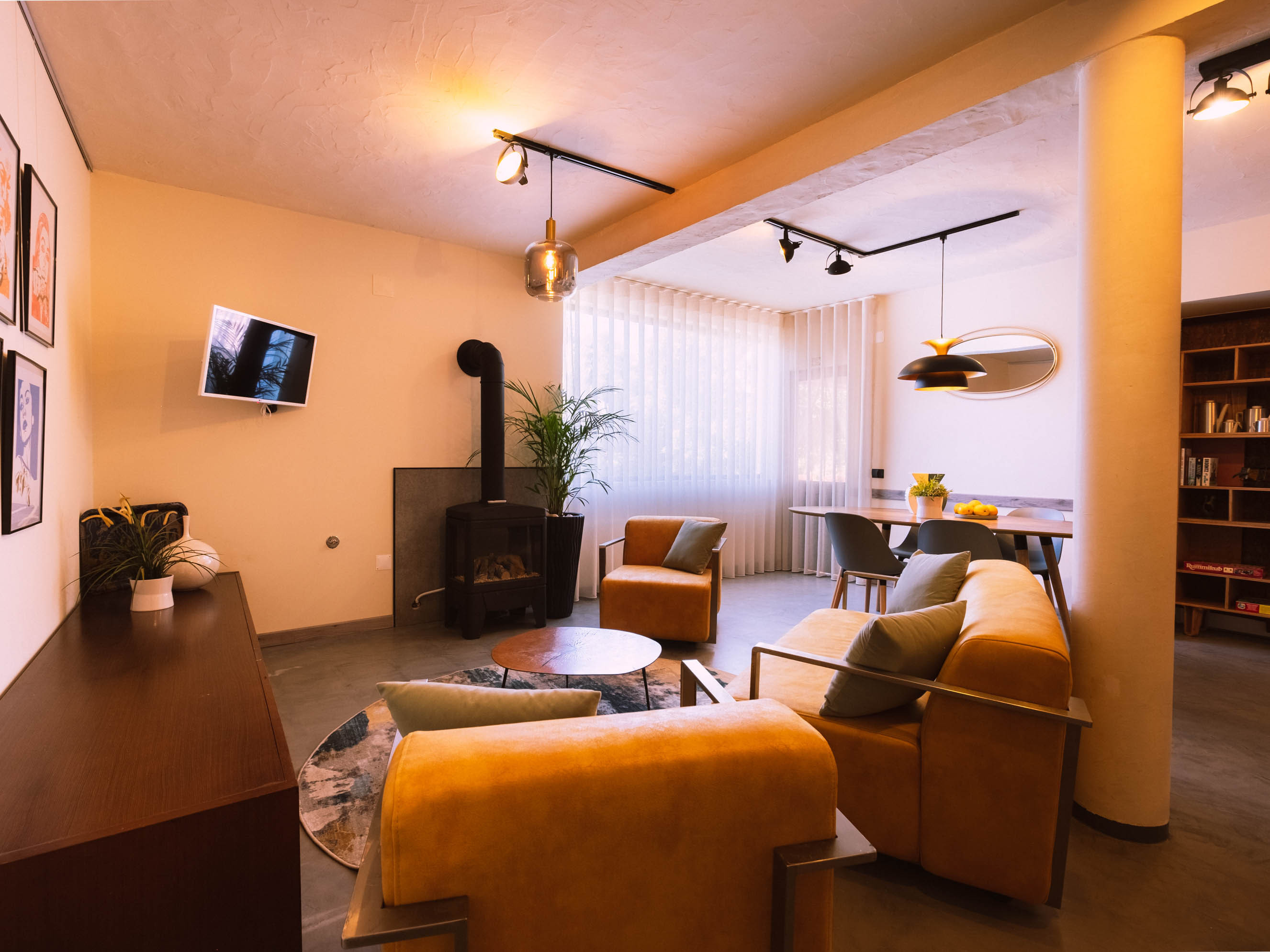 Living room with mustard yellow sofas, round coffee table, wood stove, and dining area with modern chairs.