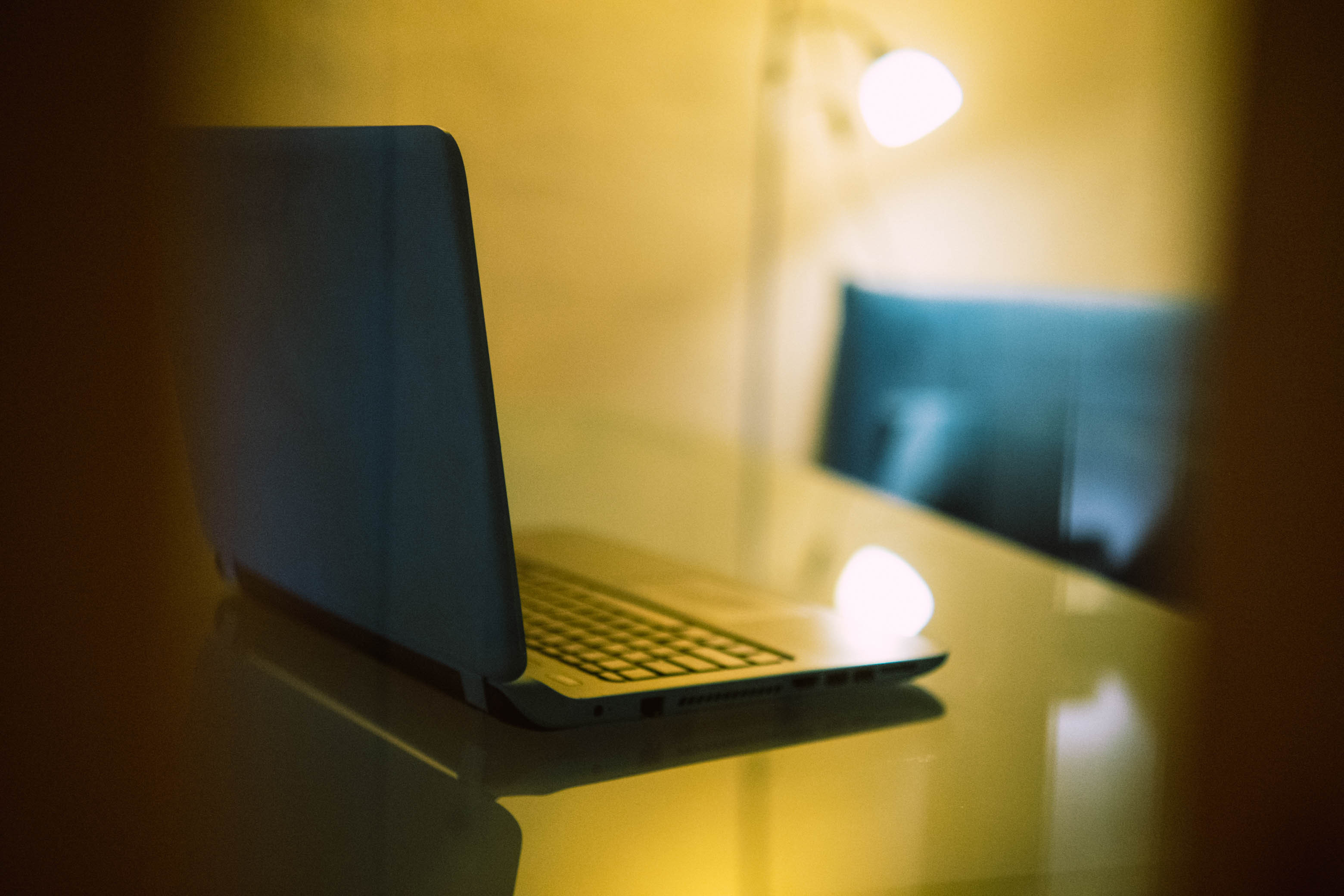 Laptop partially open on a reflective surface with warm indoor lighting in background.
