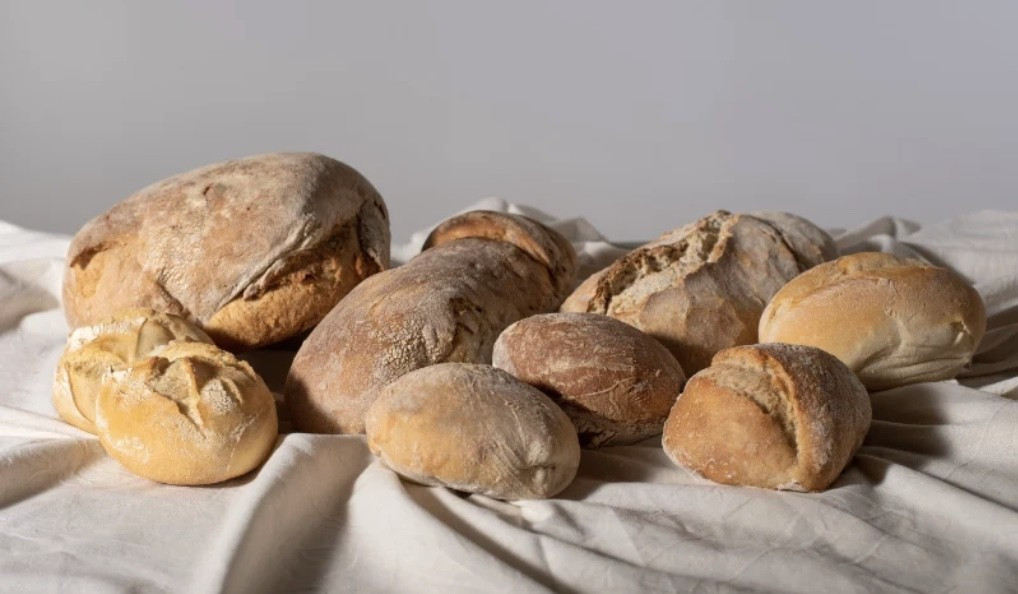Several different types of rustic bread loaves arranged on a white cloth surface.