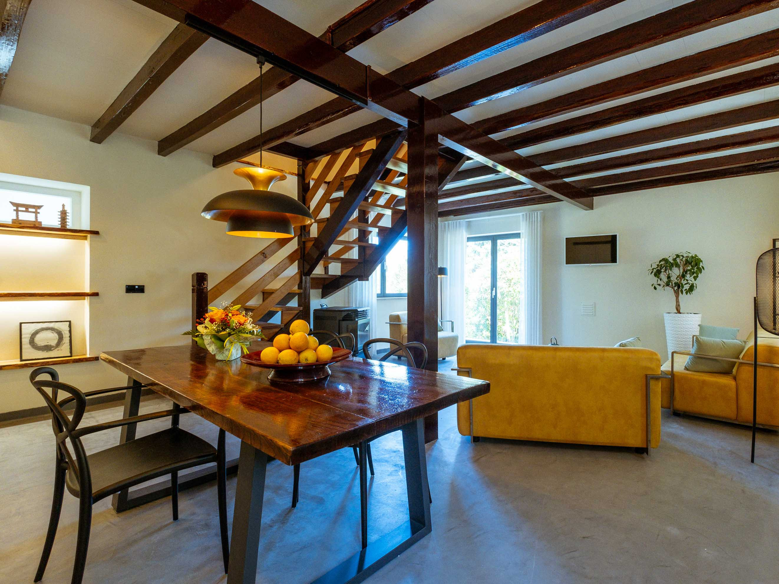 Dining area with wooden table, black chairs, modern pendant lights, and adjacent living room with yellow couches.