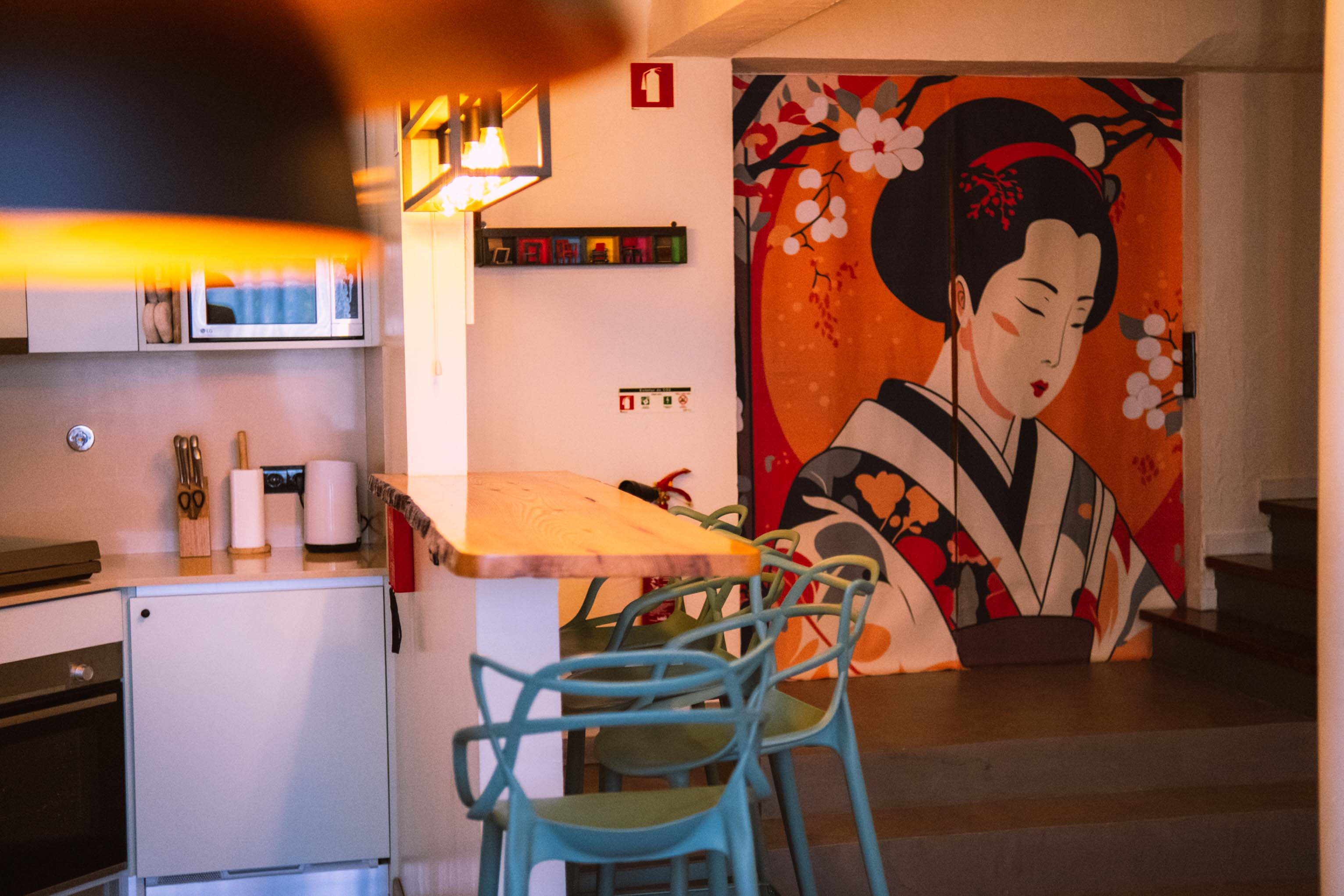 Modern kitchen area with wooden counter, blue chairs, and large colorful painting of a woman in traditional attire.