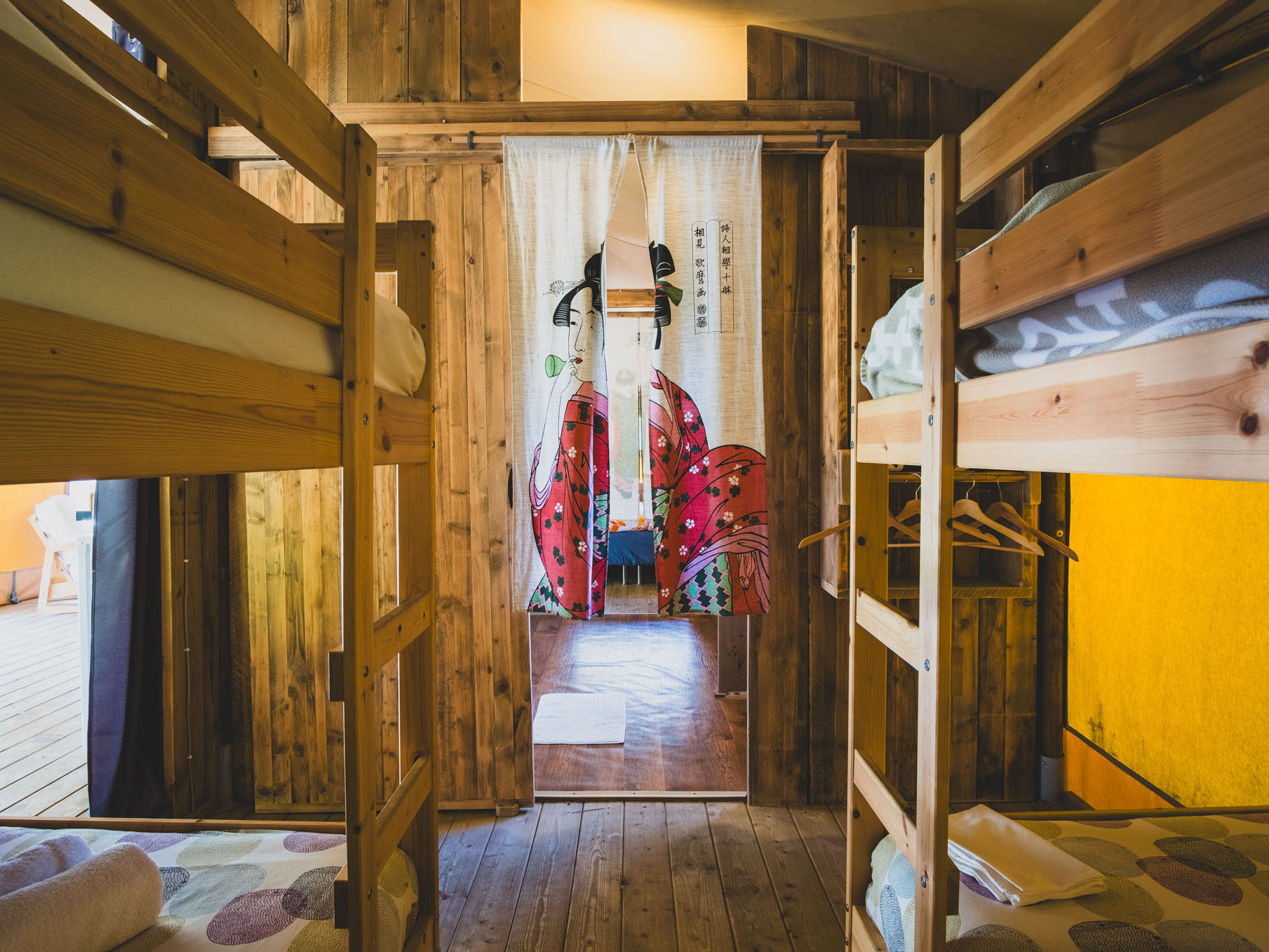 Wooden bunk beds in a room with wooden walls and a fabric curtain featuring a woman in traditional
