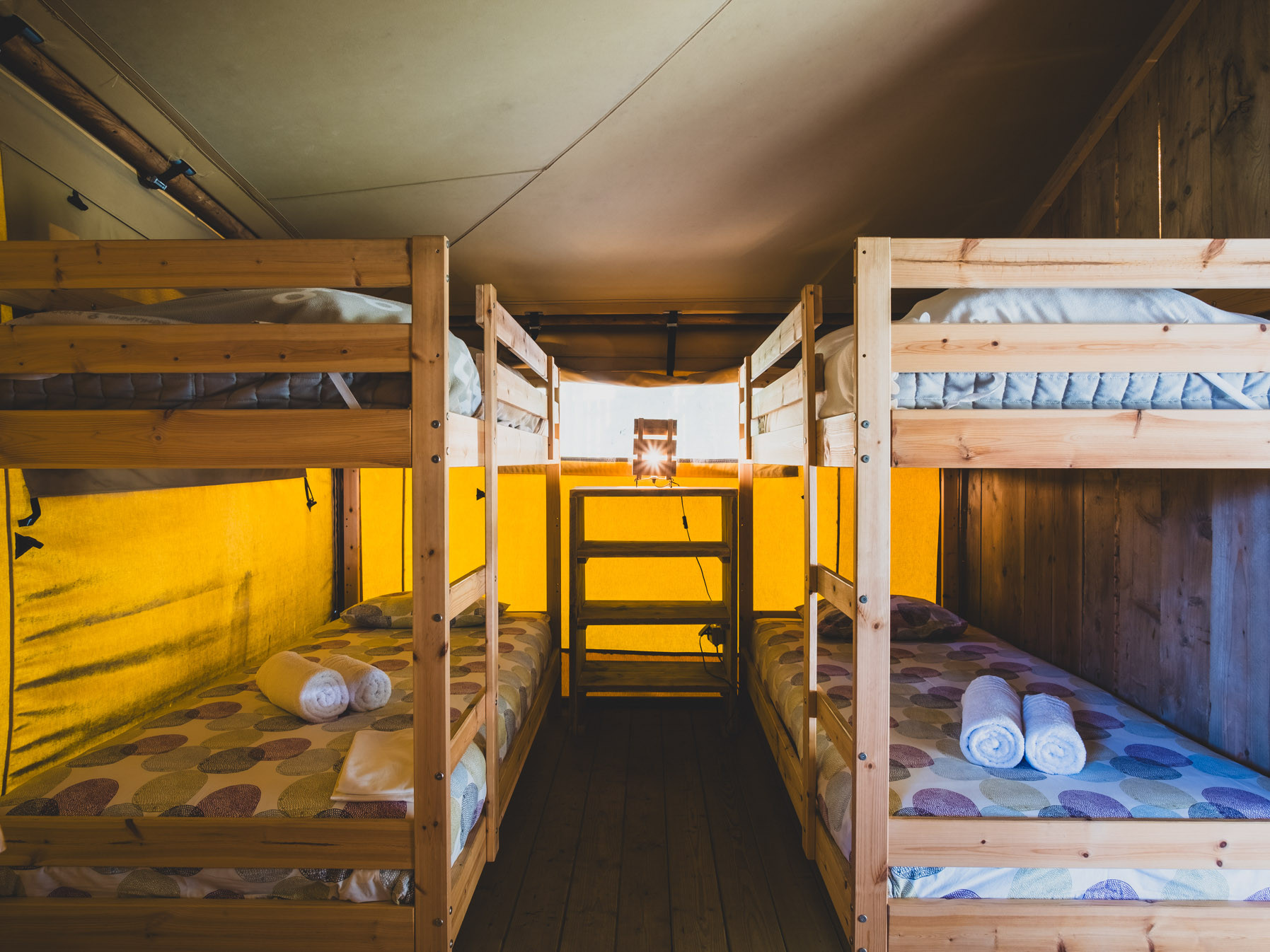 Interior of a tent with two sets of wooden bunk beds and a small table with a lamp