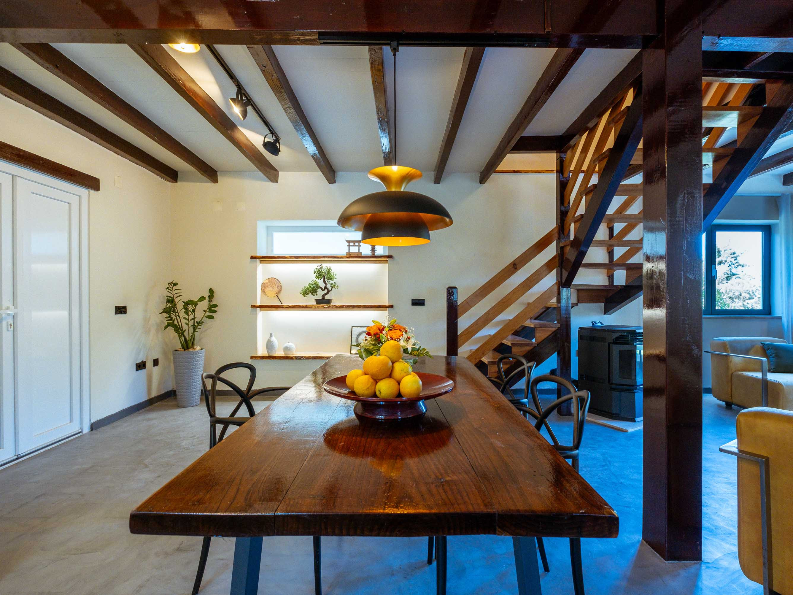 Wooden dining table with a bowl of lemons under a hanging light in a room with exposed ceiling