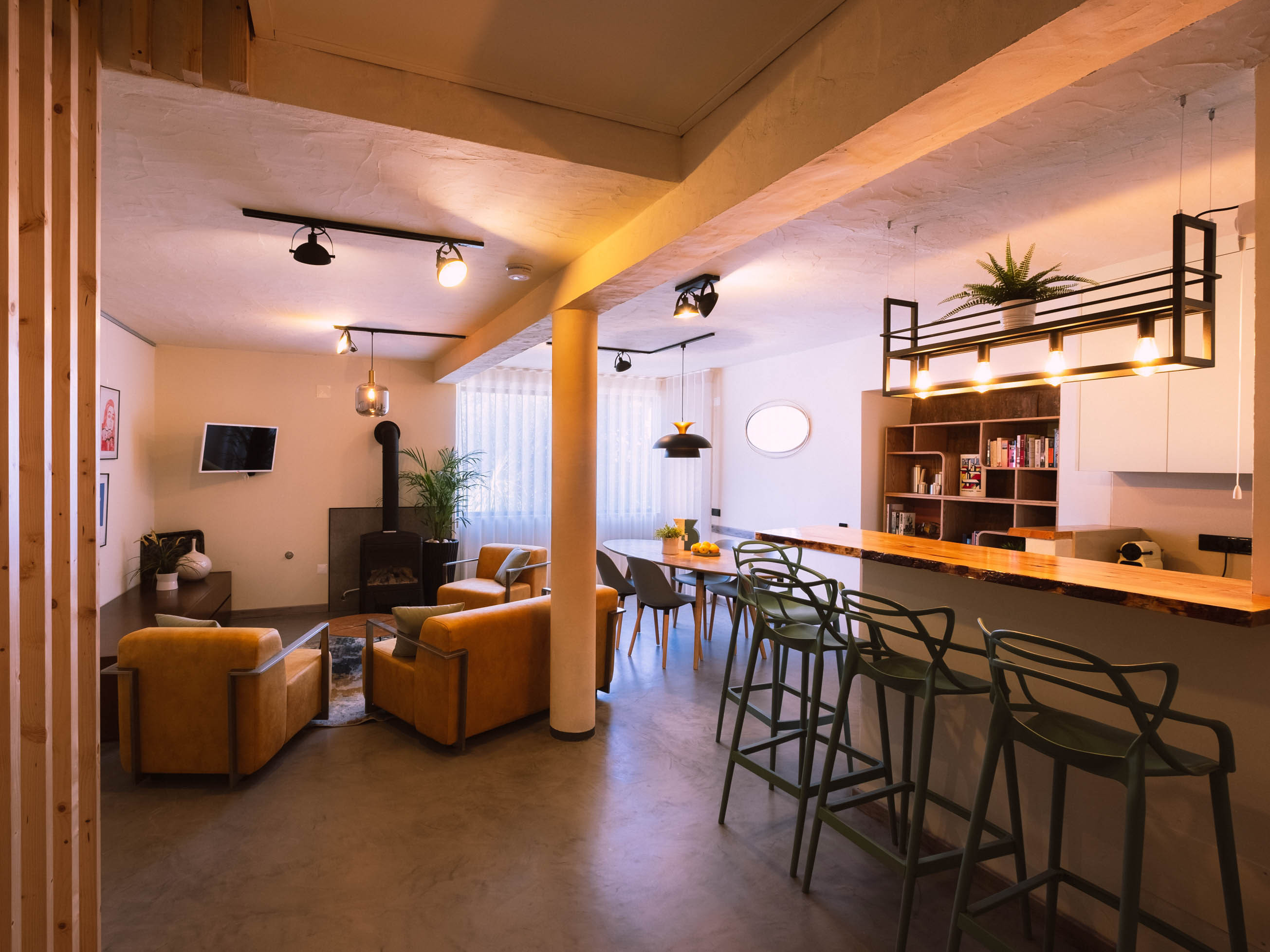 Open living space with brown armchairs, dining table, bar counter with stools, and modern lighting fixtures.