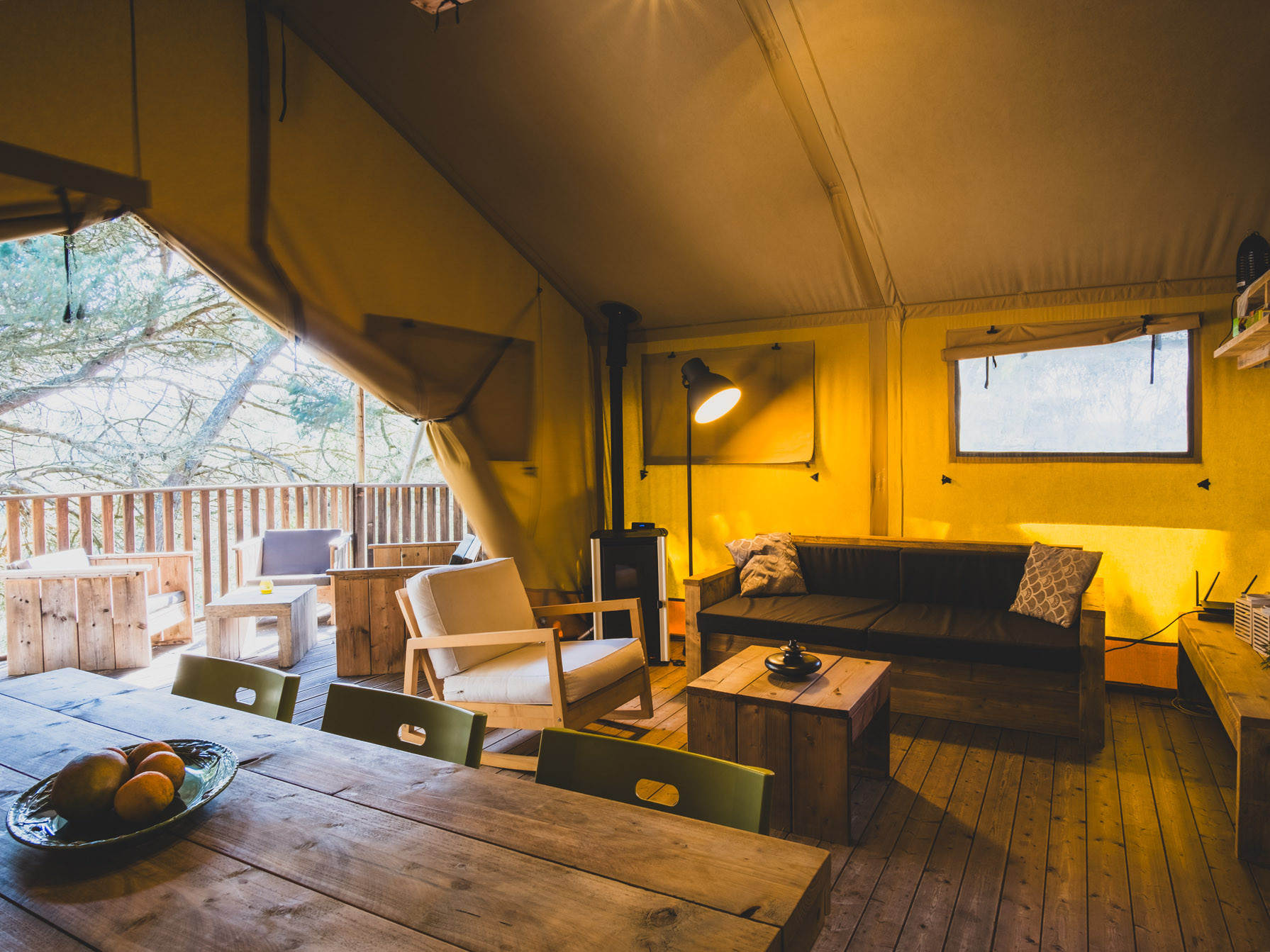 Interior of a tent with wooden furniture, a sofa, armchair, and dining table with fruit bowl.