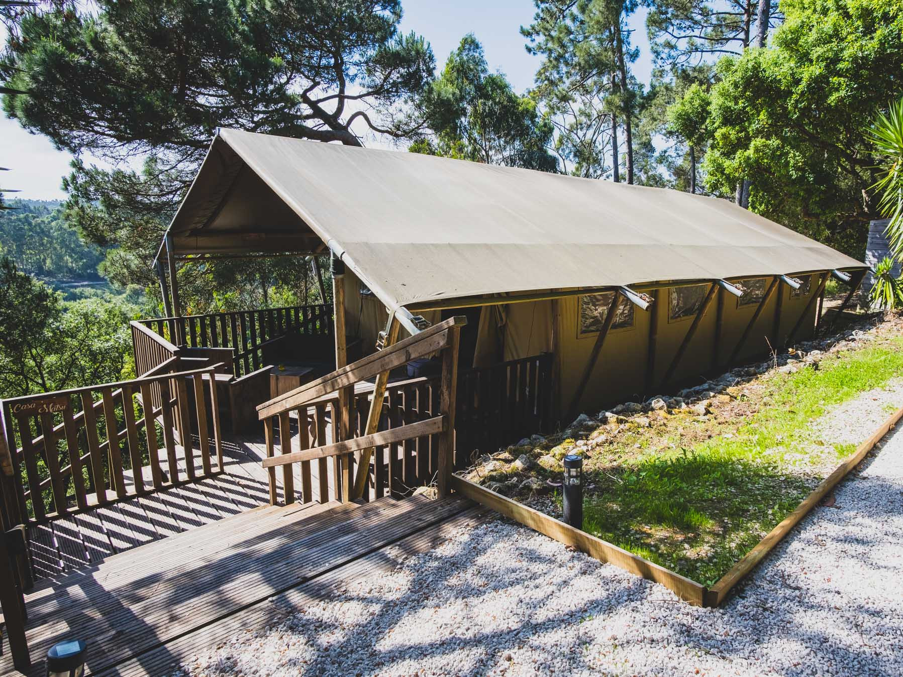 Large beige tent with wooden deck surrounded by trees and greenery on a sunny day