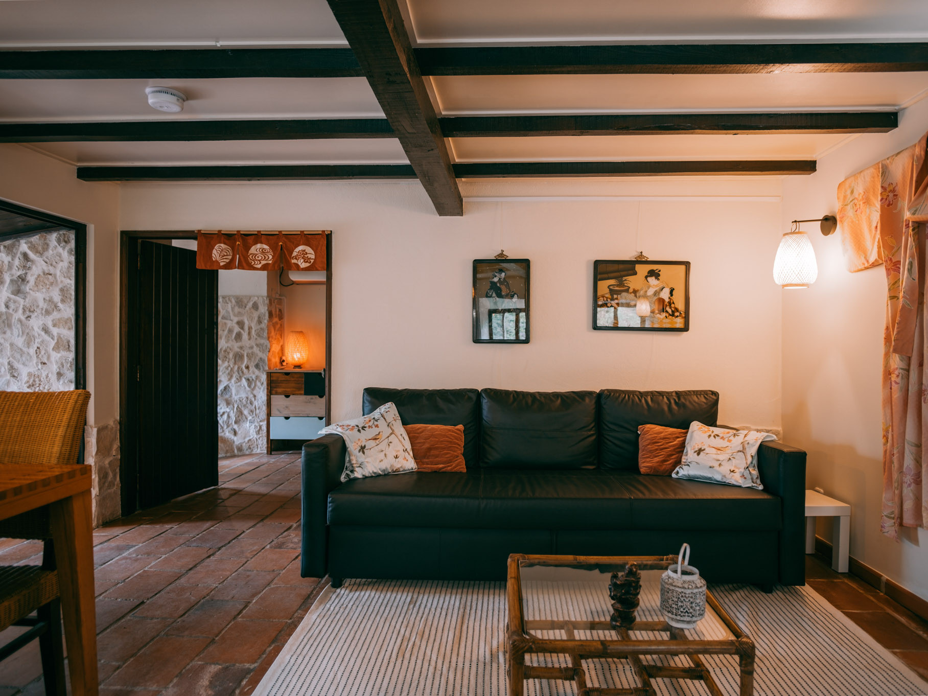 Living room with black leather sofa, decorative pillows, framed pictures, wooden beams, and a small coffee table.
