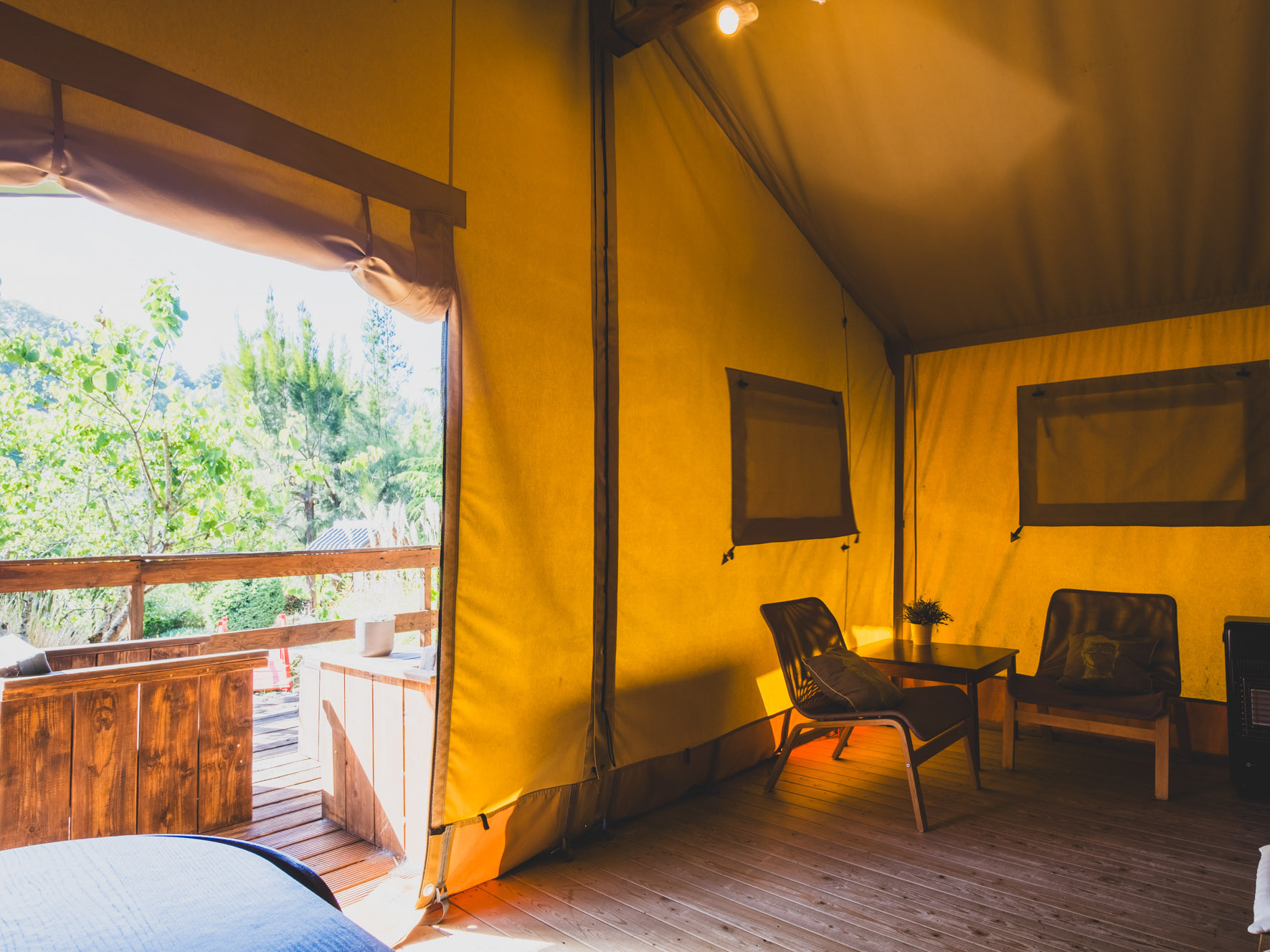 Interior of a yellow fabric tent with wooden floor, two chairs, a table, and an open entrance
